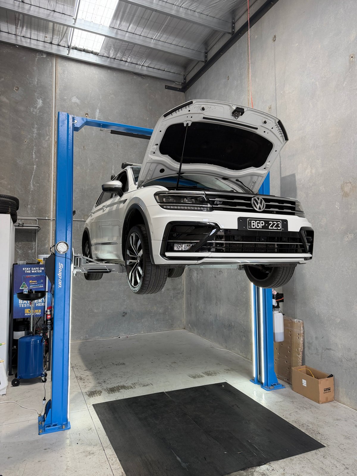 White Volkswagen vehicle lifted on a blue two-post car lift in an industrial garage with concrete walls