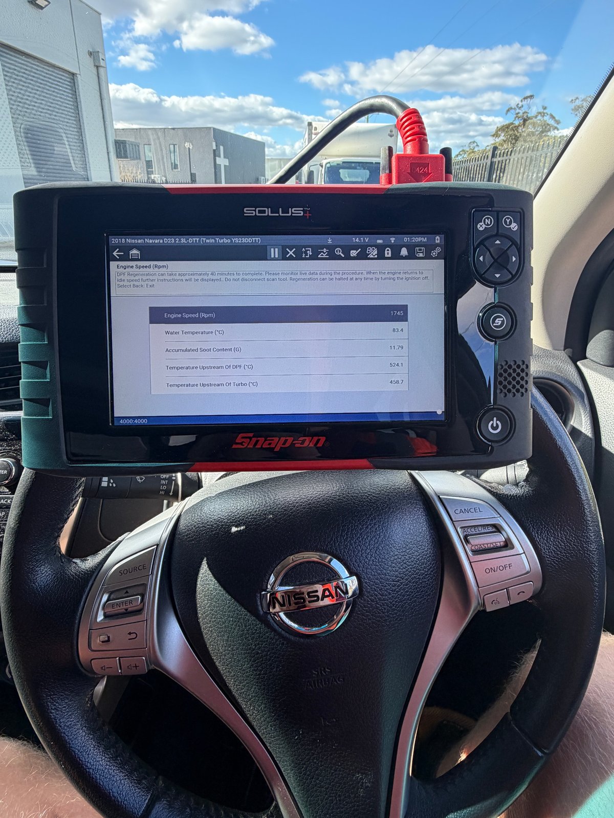 Snap-on diagnostic scanner mounted on Nissan vehicle steering wheel displaying system data on screen