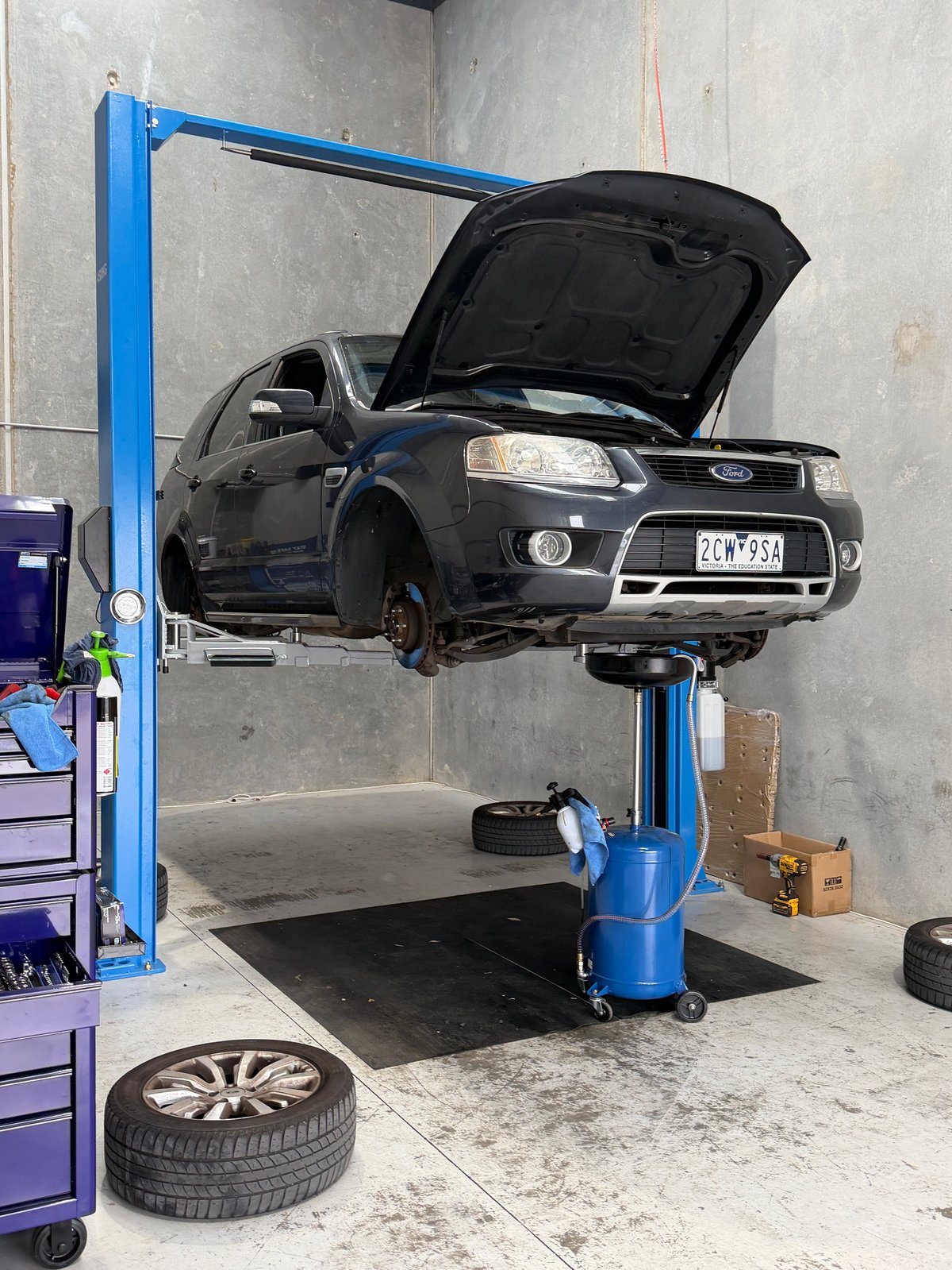 Black Ford SUV lifted on blue hydraulic car lift in automotive repair shop with hood open