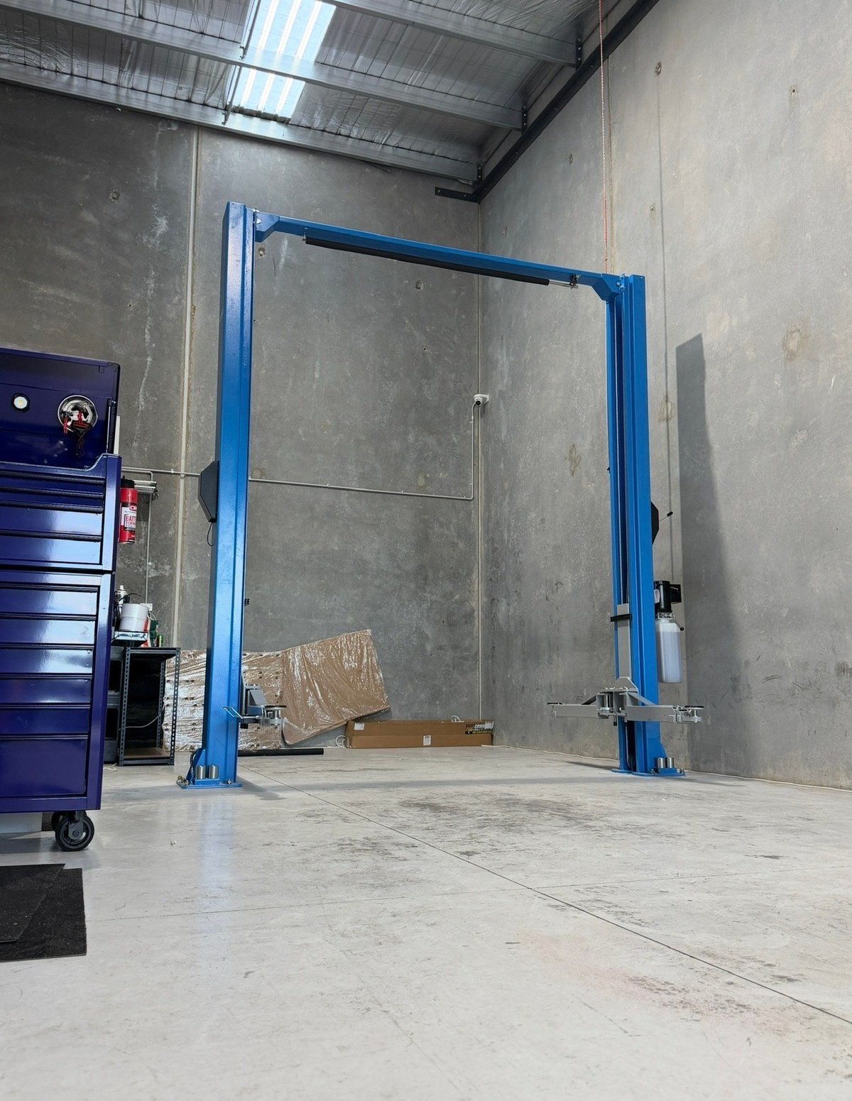 Blue two-post vehicle lift in an industrial garage workshop with concrete floor and metal walls